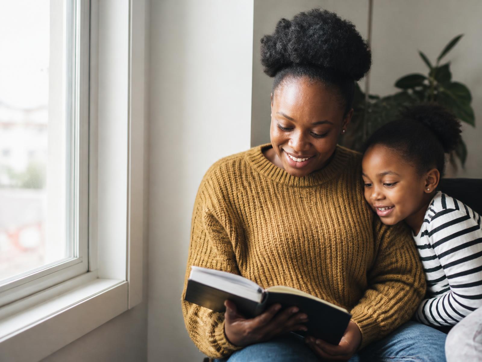 A young Black mother reading with her daughter by a window